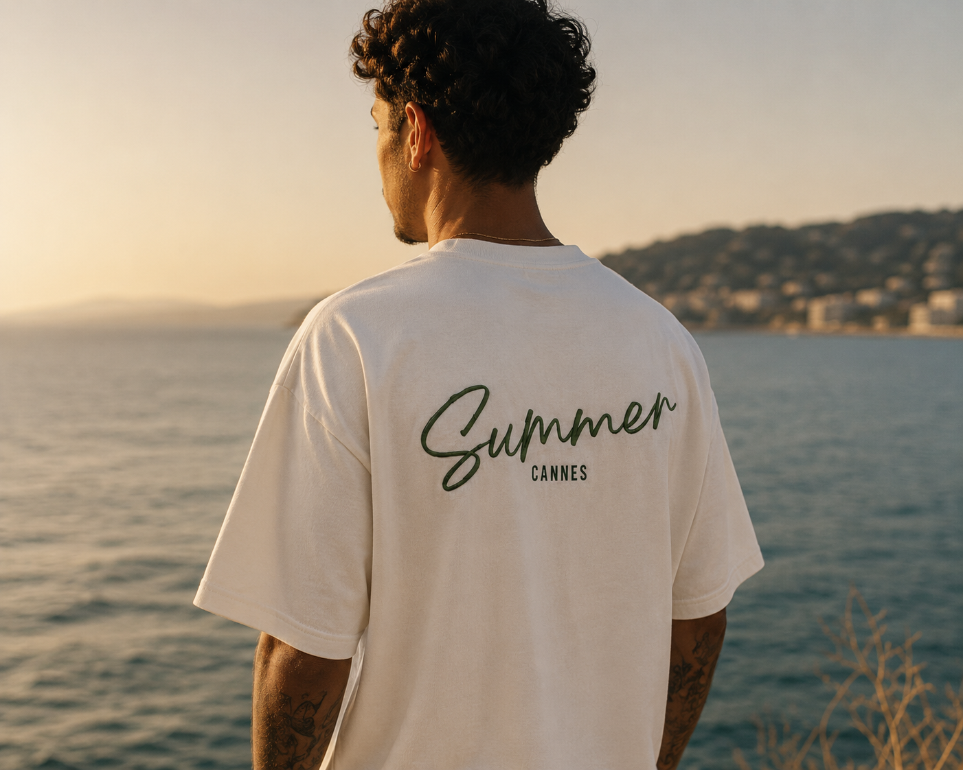 Rear view of an off-white Summer Cannes t-shirt against the sea at sunset