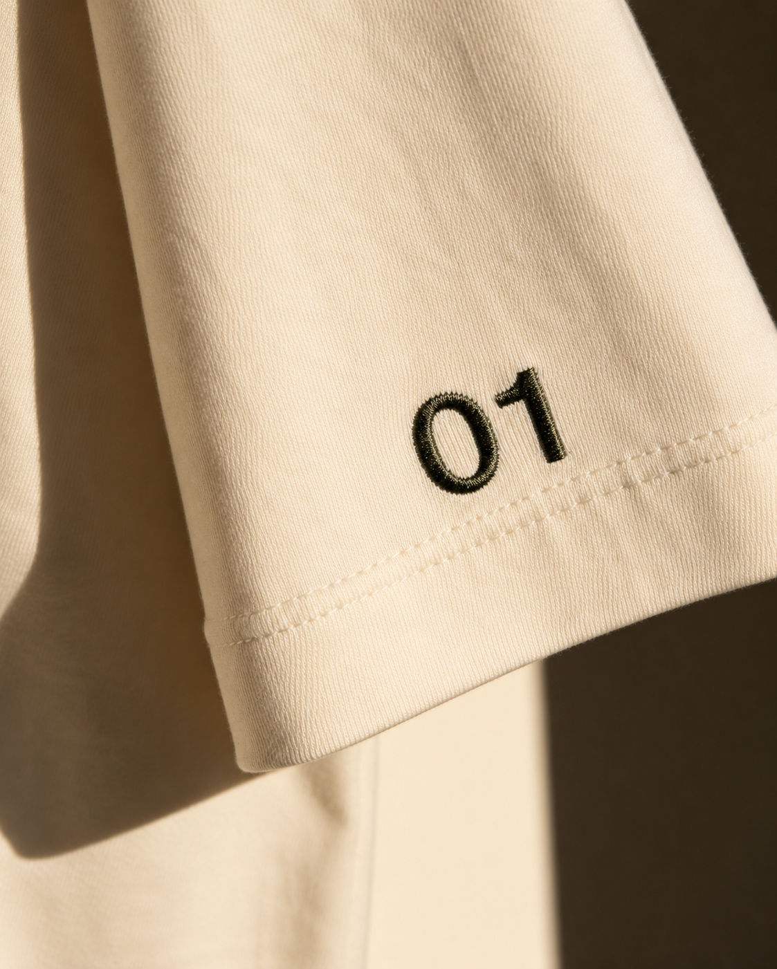 Close-up of the embroidered 01 number on the sleeve of a cream tee