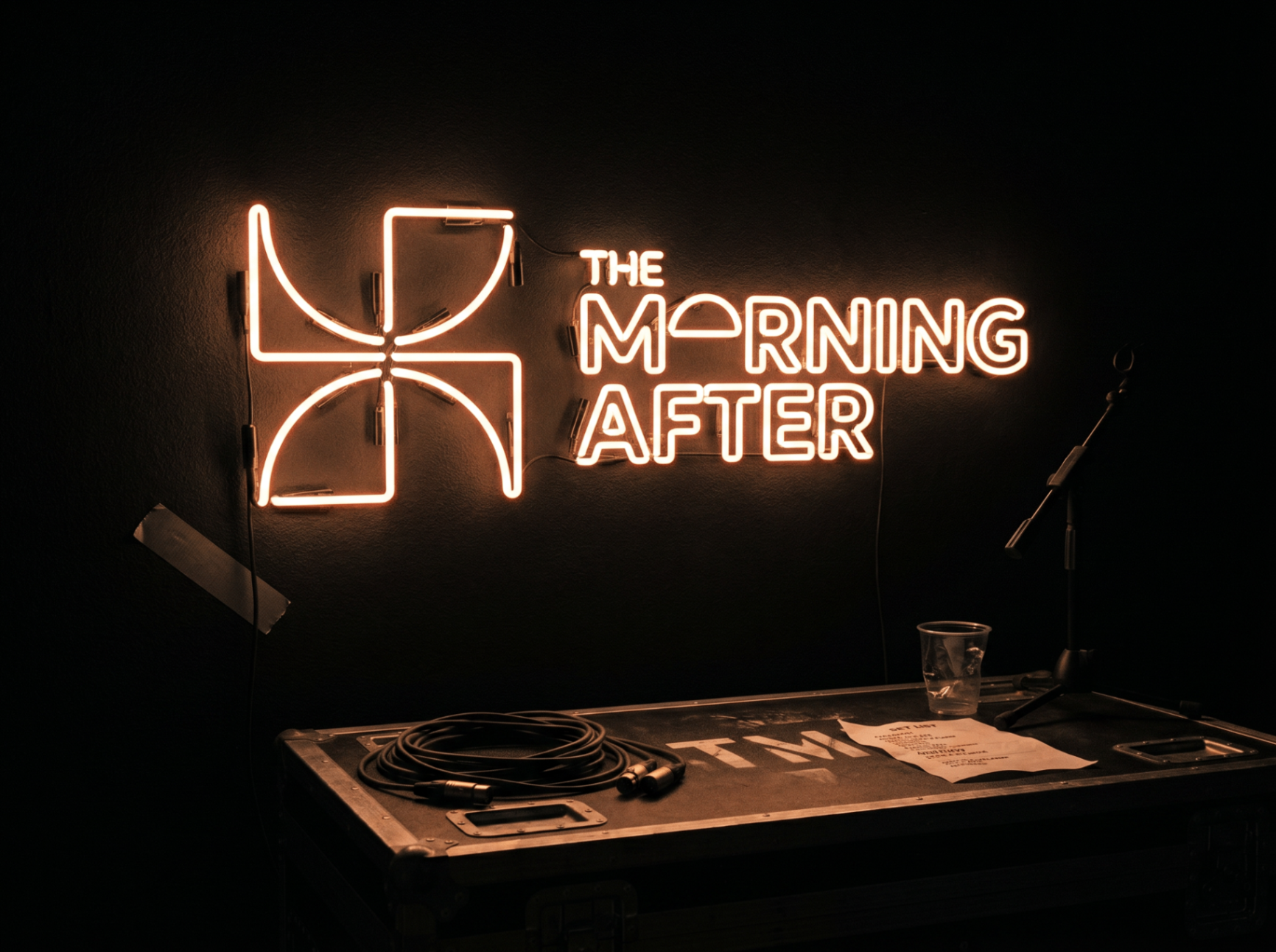 A glowing THE MORNING AFTER neon sign mounted on a dark wall above a DJ booth