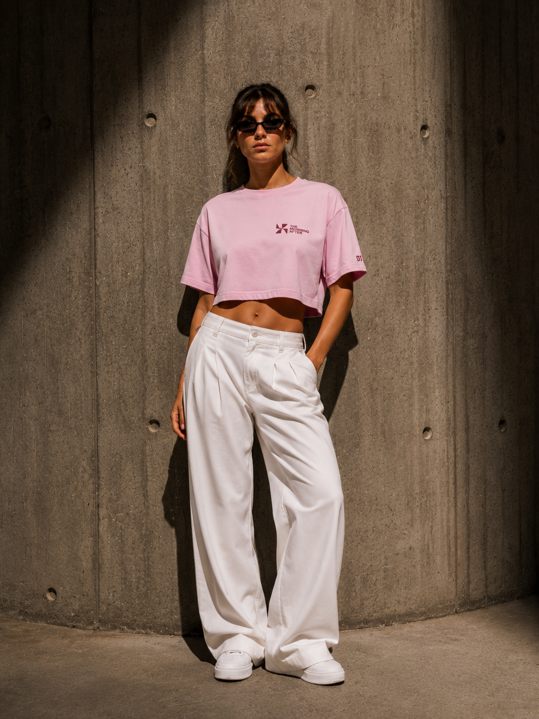 Model wearing a pink The Morning After crop top and white trousers against a concrete wall