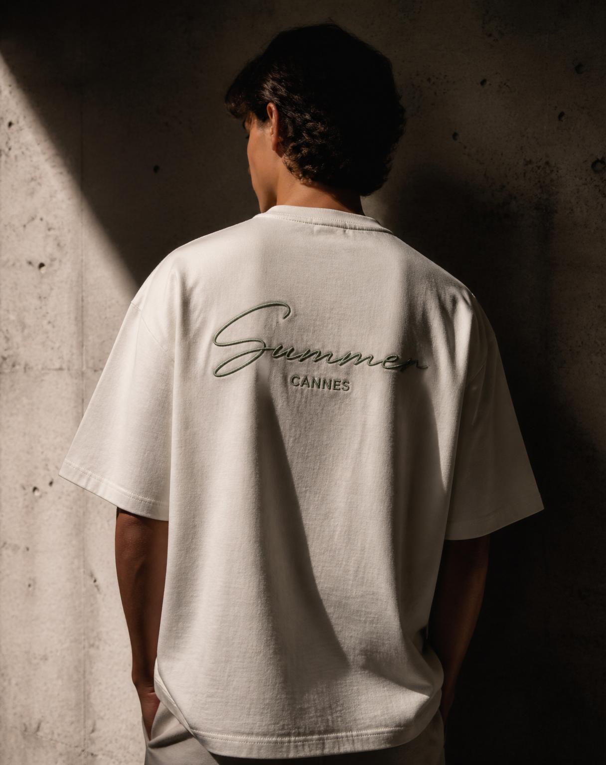 A model seen from behind wearing the Summer tee against a raw concrete wall in soft Riviera light